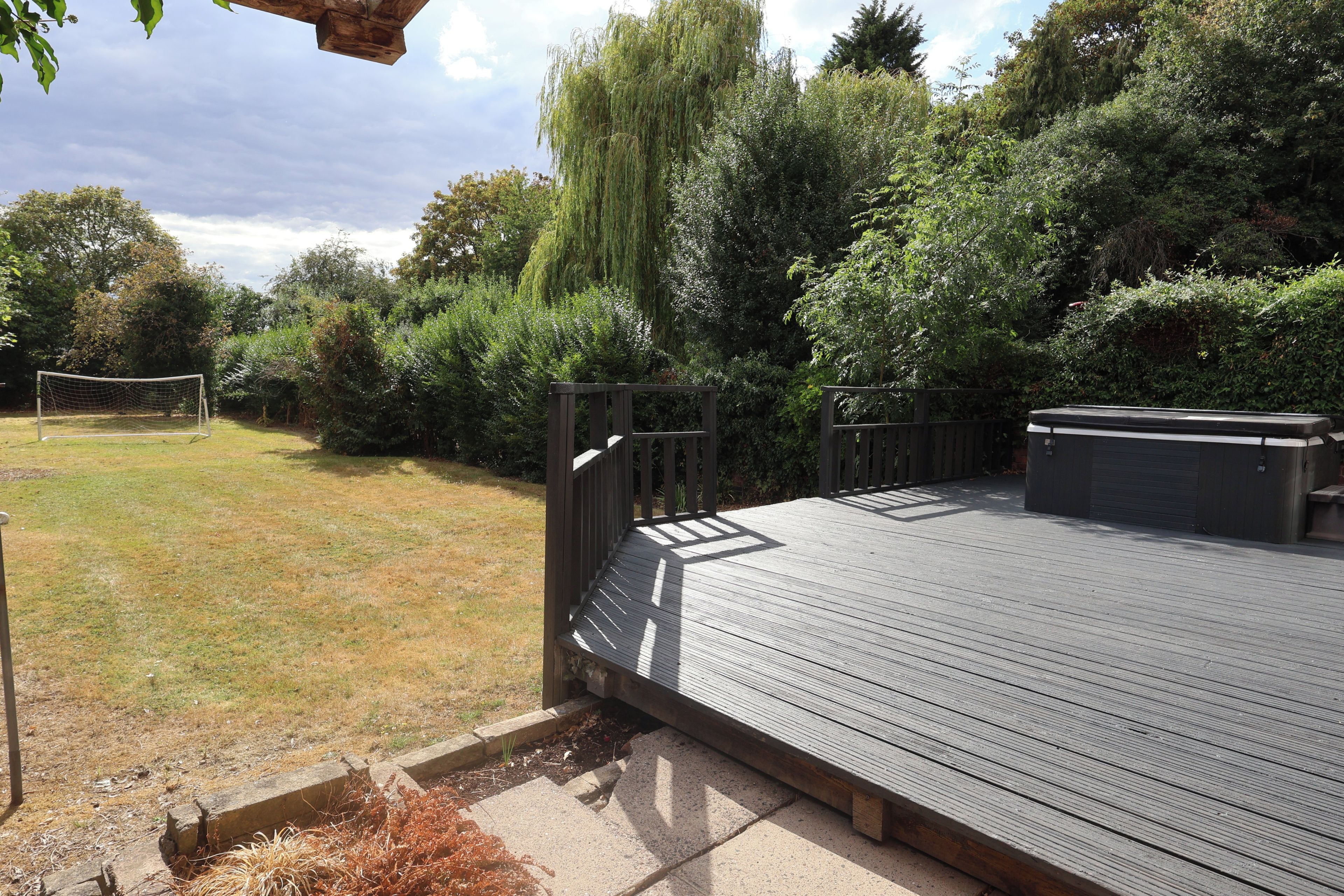 A wooden deck with a metal railing, surrounded by a garden with various plants and a tree.