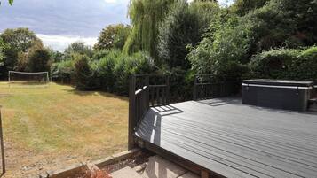 A wooden deck with a metal railing, surrounded by a garden with various plants and a tree.