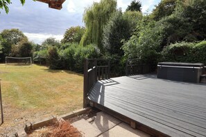 Una terraza de madera con baranda de metal, rodeada por un jardín con diversas plantas y un árbol.