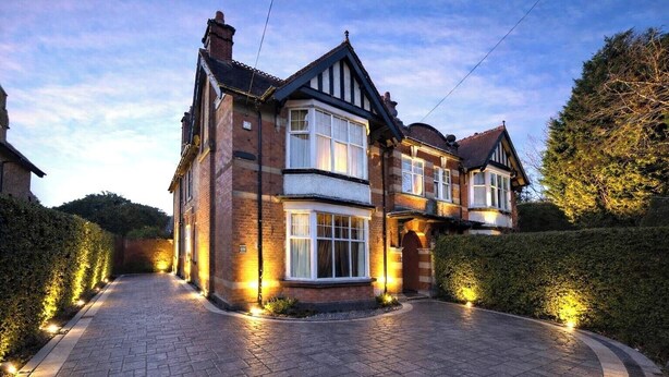 A two-story house with a driveway and hedges.