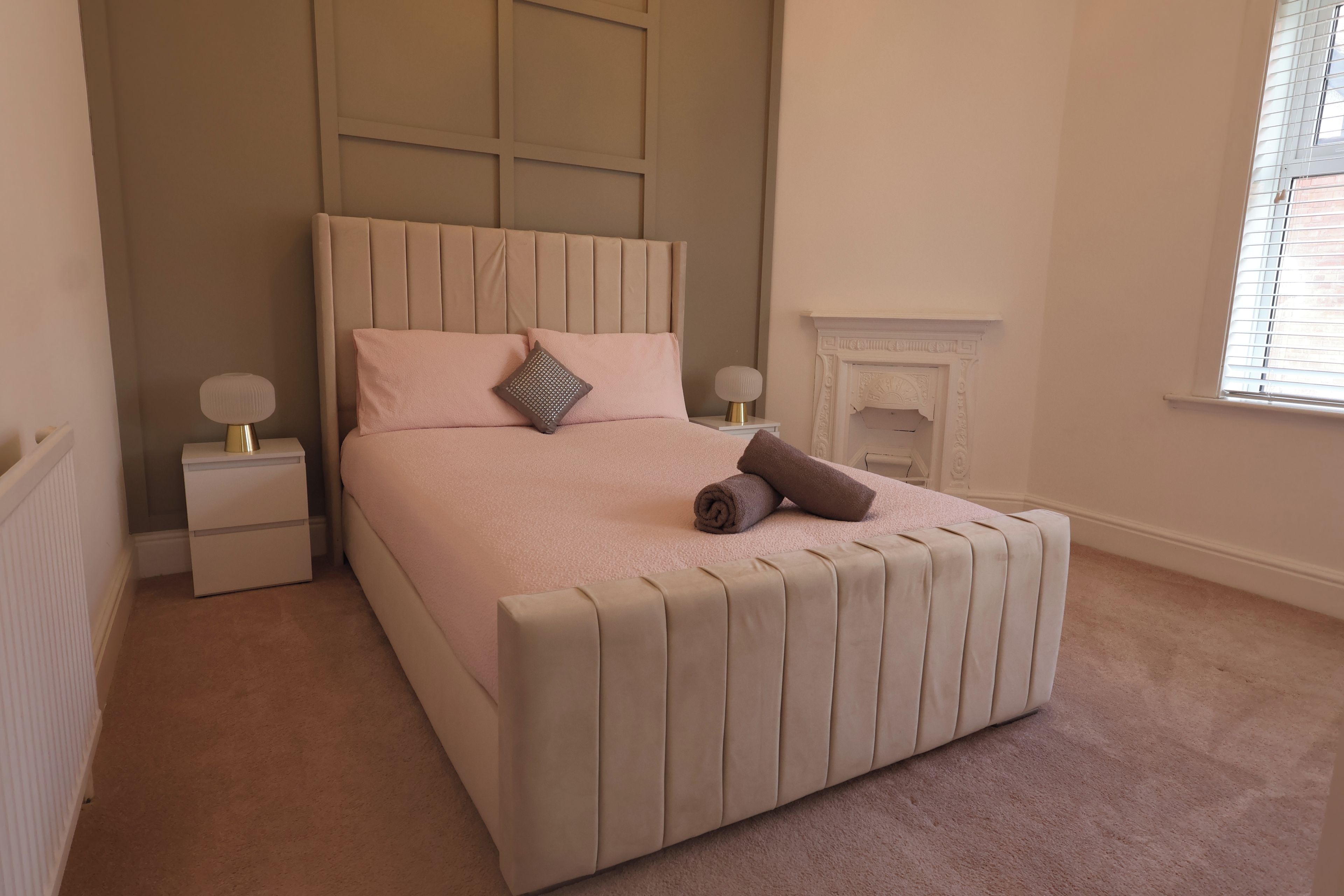 Une chambre à coucher avec un lit, des tables de chevet, une cheminée et une fenêtre.