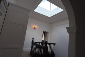 A staircase with a skylight leading to a second floor, a wall-mounted light fixture, and a door at the top of the stairs.