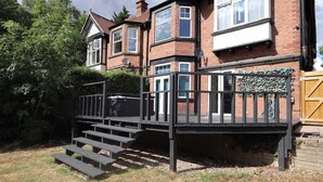 Una propiedad residencial con una casa de ladrillo de dos pisos, una terraza de madera con escalones y un acceso con portón.