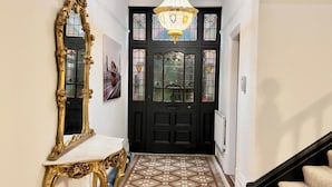 A hallway with a black door, a gold-framed mirror, a chandelier, and a patterned floor.