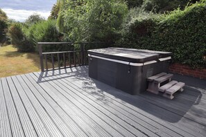 A hot tub on a wooden deck with a metal railing and a brick wall in the background.