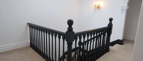 A staircase with black balusters and a handrail, carpeted steps, and a wall-mounted light fixture.