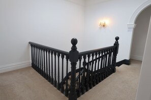 A staircase with black balusters and a handrail, carpeted steps, and a wall-mounted light fixture.