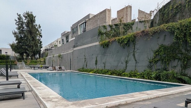 Ein rechteckiger Swimmingpool mit Fliesenrand, umgeben von Liegestühlen und einer Betonmauer mit Bepflanzung.