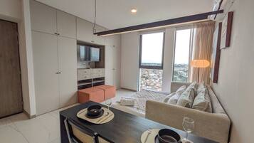 A modern living space with a dining area, a sofa, a television, and a view of the city.