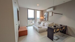 Ein modernes Hotelzimmer mit Bett, Esstisch mit Stühlen, einer Sitzecke und Blick auf die Stadt.