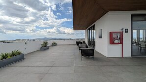 Eine Dachterrasse mit Sitzgelegenheiten, einem Feuerlöscher und Blick auf die Stadtlandschaft.