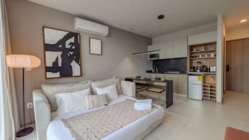 A modern hotel room with a large bed, a kitchenette, and a dining area.