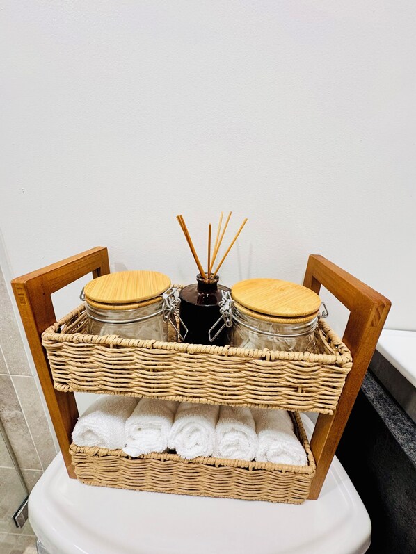 Una cesta de mimbre con dos tarros de vidrio y una botella de difusor de aroma de juncos sobre un pedestal blanco.