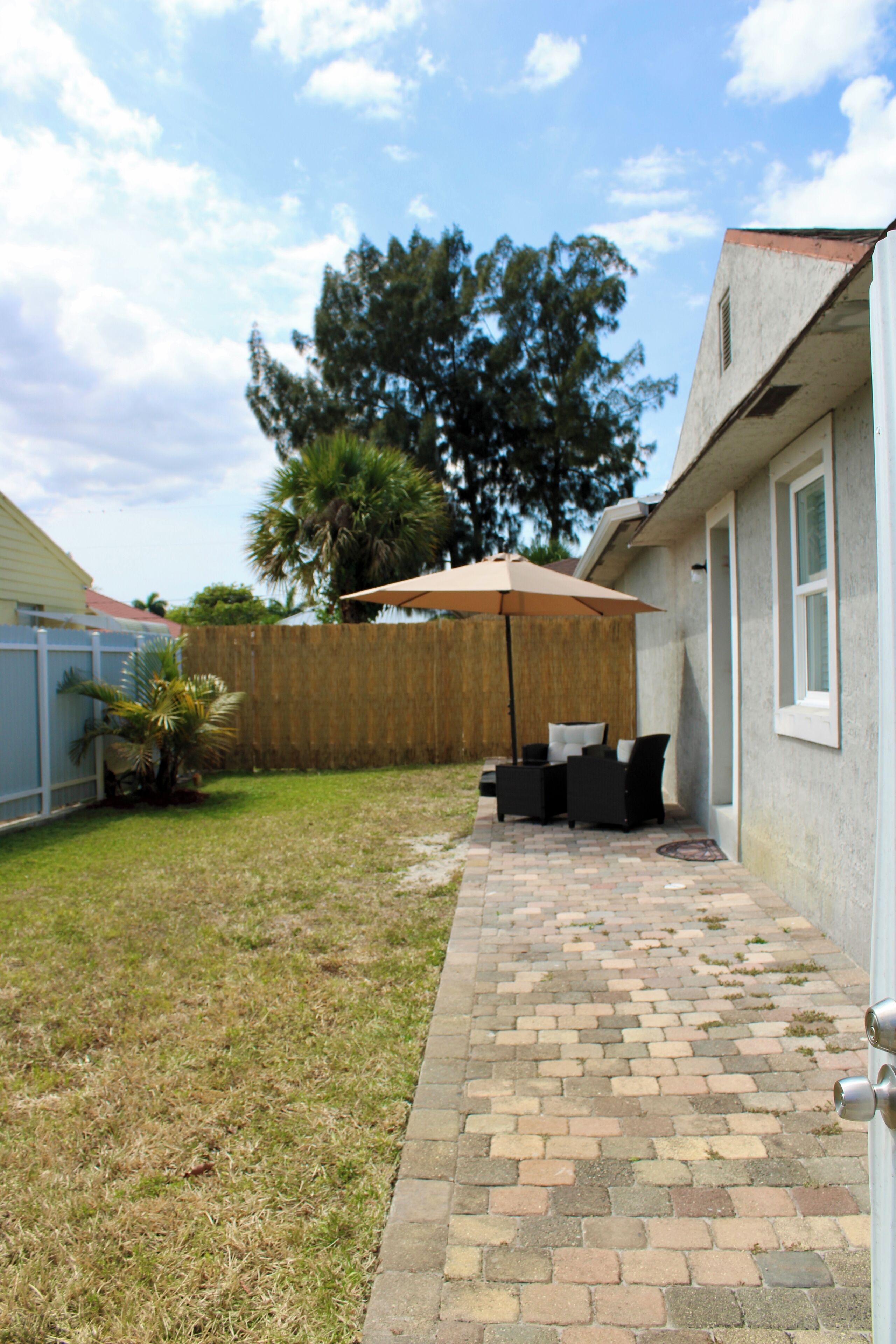 A backyard patio with a brick pathway, a wooden fence, and a patio umbrella.