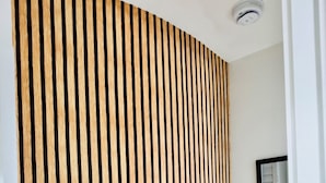 A room with a wooden slat partition, a white wall, a ceiling light, and a window with blinds.