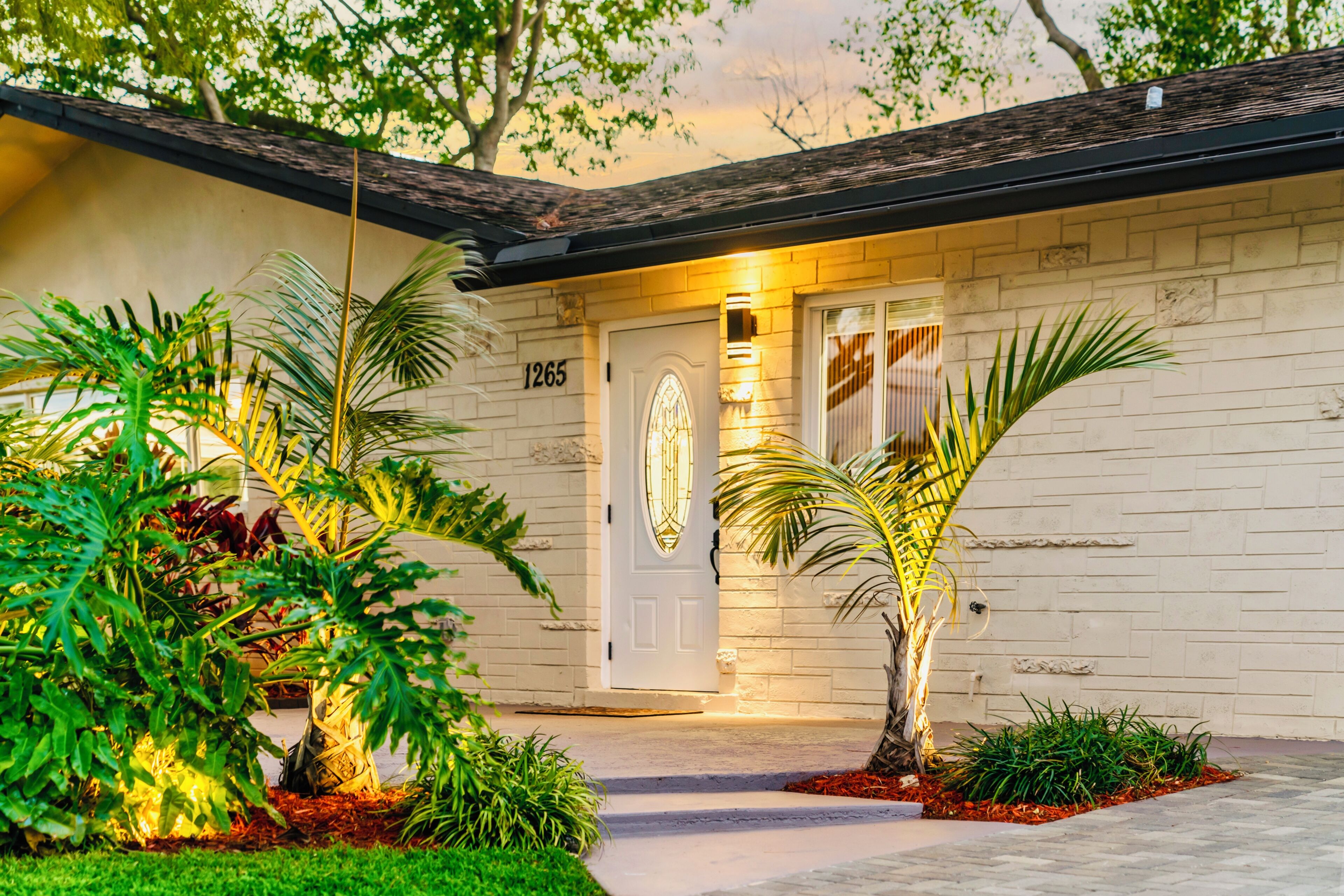A house with a white exterior, a number '1265' on the door, and a well-lit entrance.