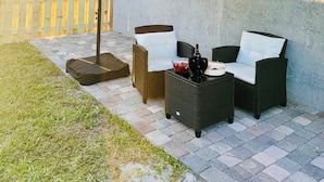 An outdoor patio area with wicker furniture, a large umbrella, and a wooden fence.