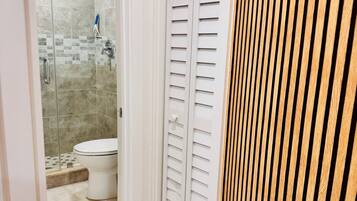A bathroom with a shower, toilet, and a white door with louvered panels.