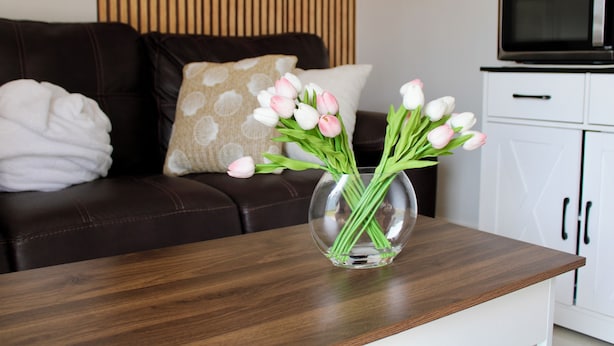 A living room with a dark brown leather sofa, a glass vase with white and pink tulips, and a white cabinet with a microwave.