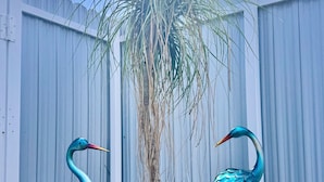 Two decorative bird sculptures in a garden area with a metal fence and mulch.