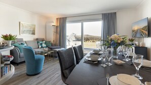 A modern hotel room with a dining area, a sofa set, and a large window offering a view of the beach. - An der Seedüne, App. Carpe diem - "Relax in our vacation apartment at (Unknown)