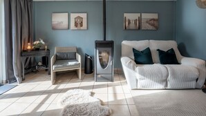 A living room with a white sofa, a wicker chair, a fireplace, and artwork on the walls. - Beluga with parking and shared pool by Interhome (De Haan)