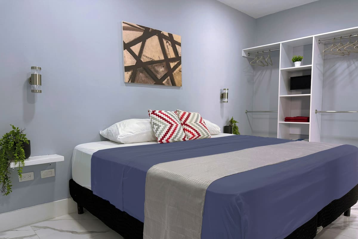 Quarto moderno com cama, pintura abstrata na parede, planta na mesa de cabeceira e armário embutido com espaço para pendurar roupas.