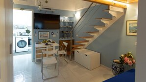 A compact kitchen with a washing machine, a dining area with chairs, and a staircase with built-in shelves.