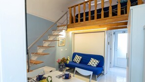A modern living room with a blue sofa, a dining table with a vase of flowers, and a staircase leading to an upper level.