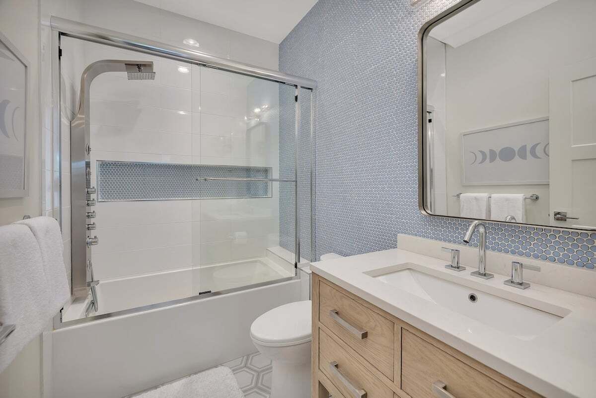 A modern bathroom with a glass-enclosed shower, a white sink with a mirror, and a tiled backsplash.