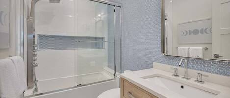 A modern bathroom with a glass-enclosed shower, a white sink with a mirror, and a tiled backsplash.