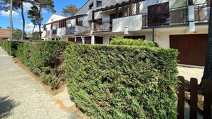 A row of modern multi-story buildings with balconies, surrounded by well-maintained hedges and trees.