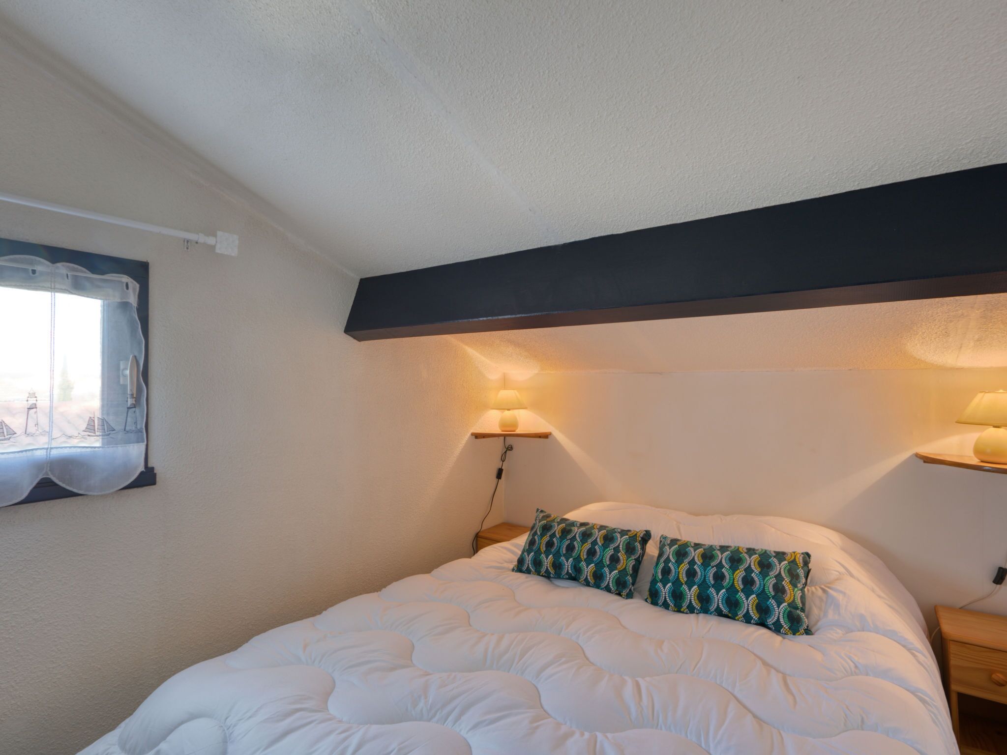 Une chambre à coucher avec un grand lit, deux lampes de chevet, une fenêtre avec un rideau et une étagère fixée au mur.