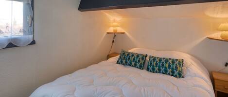 Une chambre à coucher avec un grand lit, deux lampes de chevet, une fenêtre avec un rideau et une étagère fixée au mur.