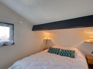 Een slaapkamer met een groot bed, twee bedlampjes, een raam met gordijn en een wandplank.