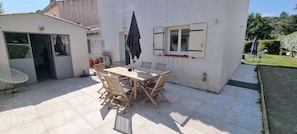Une terrasse avec une table et des chaises, un parasol et une fenêtre avec des volets.
