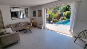 A living room with a sofa, a coffee table, a chair, a TV, a mirror, and a sliding glass door leading to a pool.