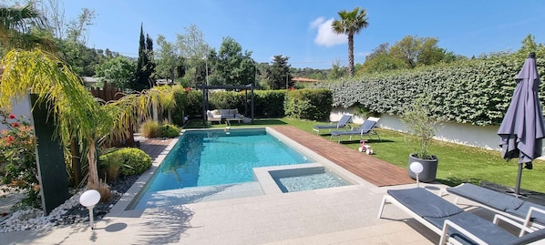 Una piscina rectangular con un deck de madera, rodeada por un jardín cuidado con diversas plantas y una pérgola.