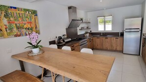 A modern kitchen with wooden cabinets, a stainless steel refrigerator, and a dining area with a wooden table and chairs.