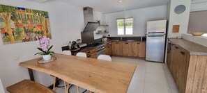 Una cocina moderna con armarios de madera, un refrigerador de acero inoxidable y una zona de comedor con mesa y sillas de madera.