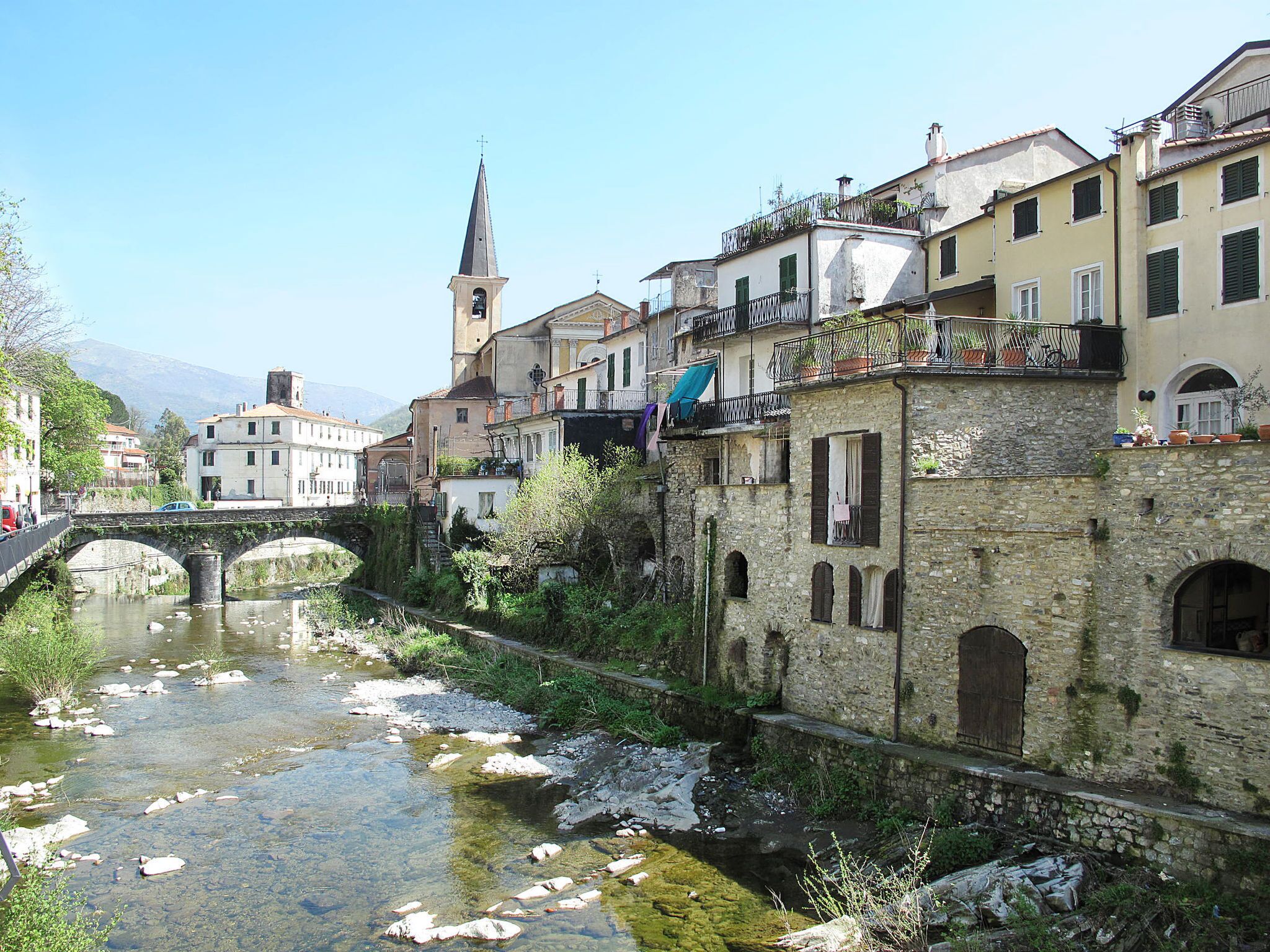 A historic town with stone buildings, a church, and a bridge over a river.