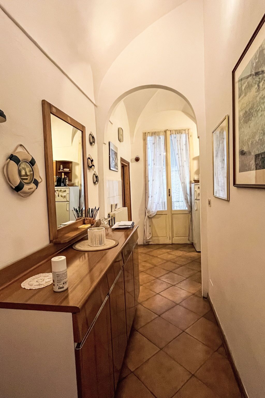 A narrow hallway with a wooden counter, a large mirror, and a door leading to a room with a tiled floor.