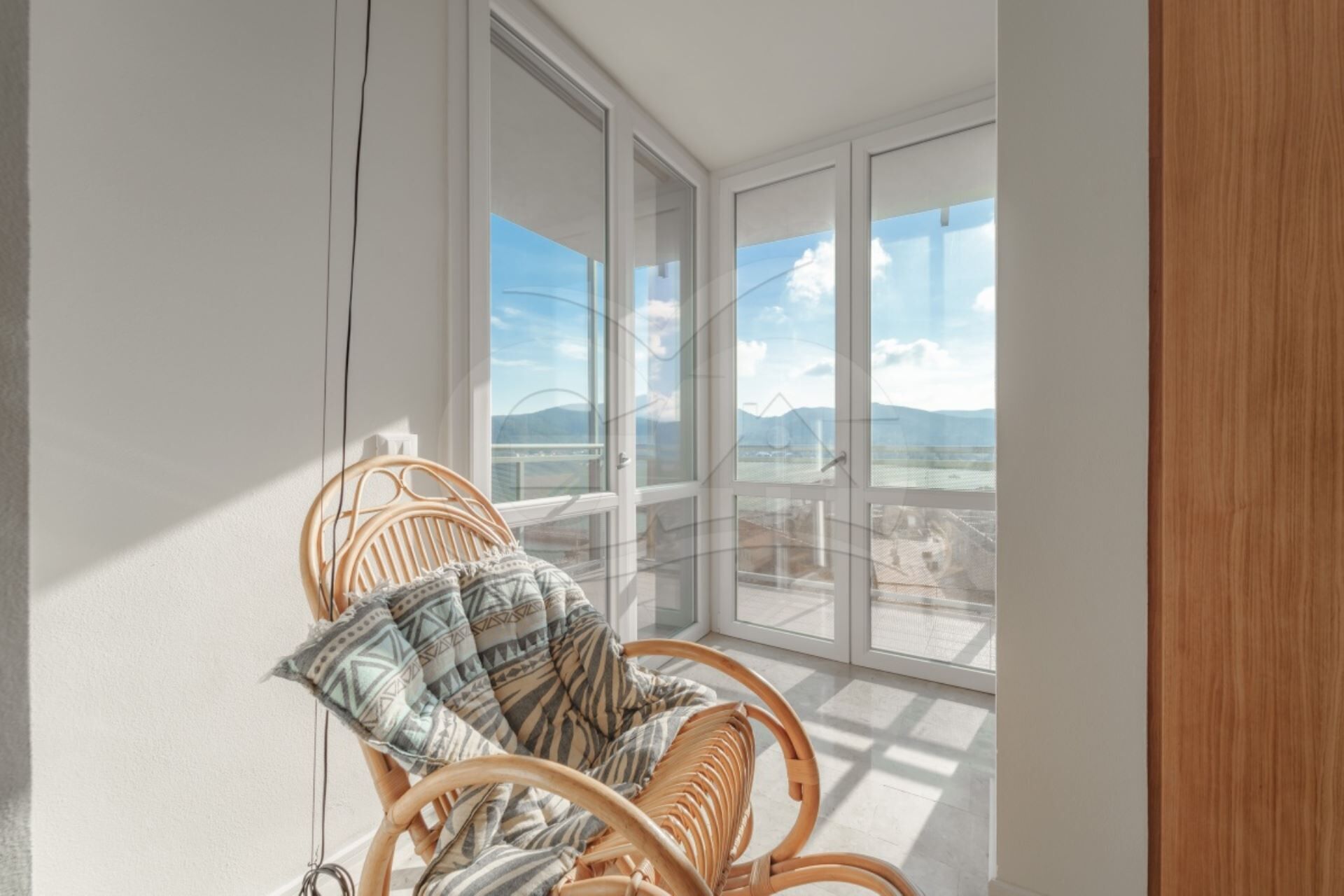 Un balcon avec un fauteuil en osier et une vue sur un paysage montagneux.