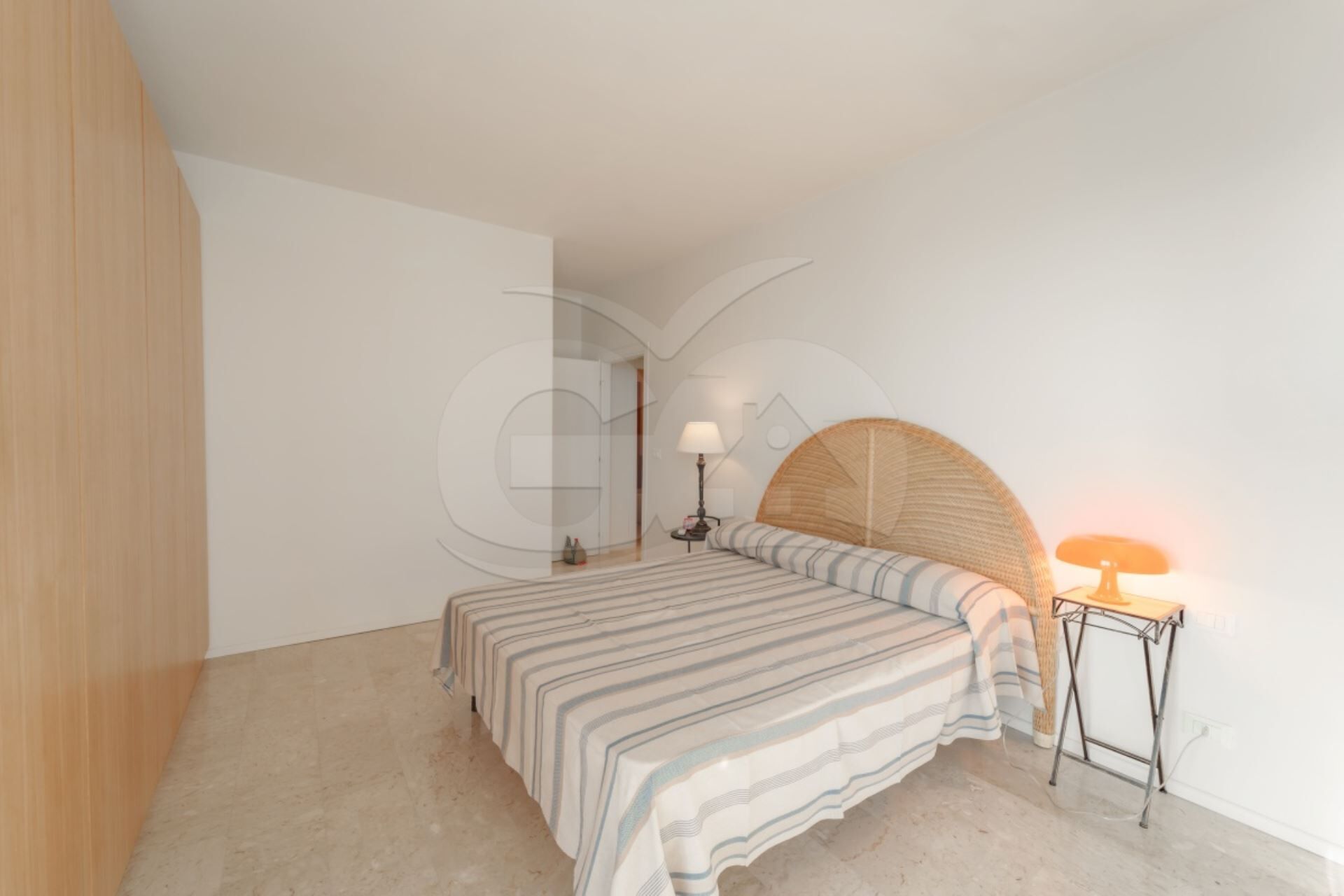 Un dormitorio con cama, una mesita de noche, una lámpara y un aplique circular en la pared.