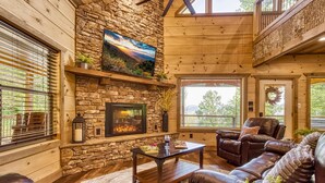 Interior acogedor de una cabaña con chimenea de piedra, muebles de cuero y un ventanal con vistas a la vegetación.