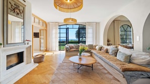Ein geräumiges Wohnzimmer mit Kamin, einer großen Couch, einem Couchtisch und Blick ins Grüne durch ein großes Fenster.