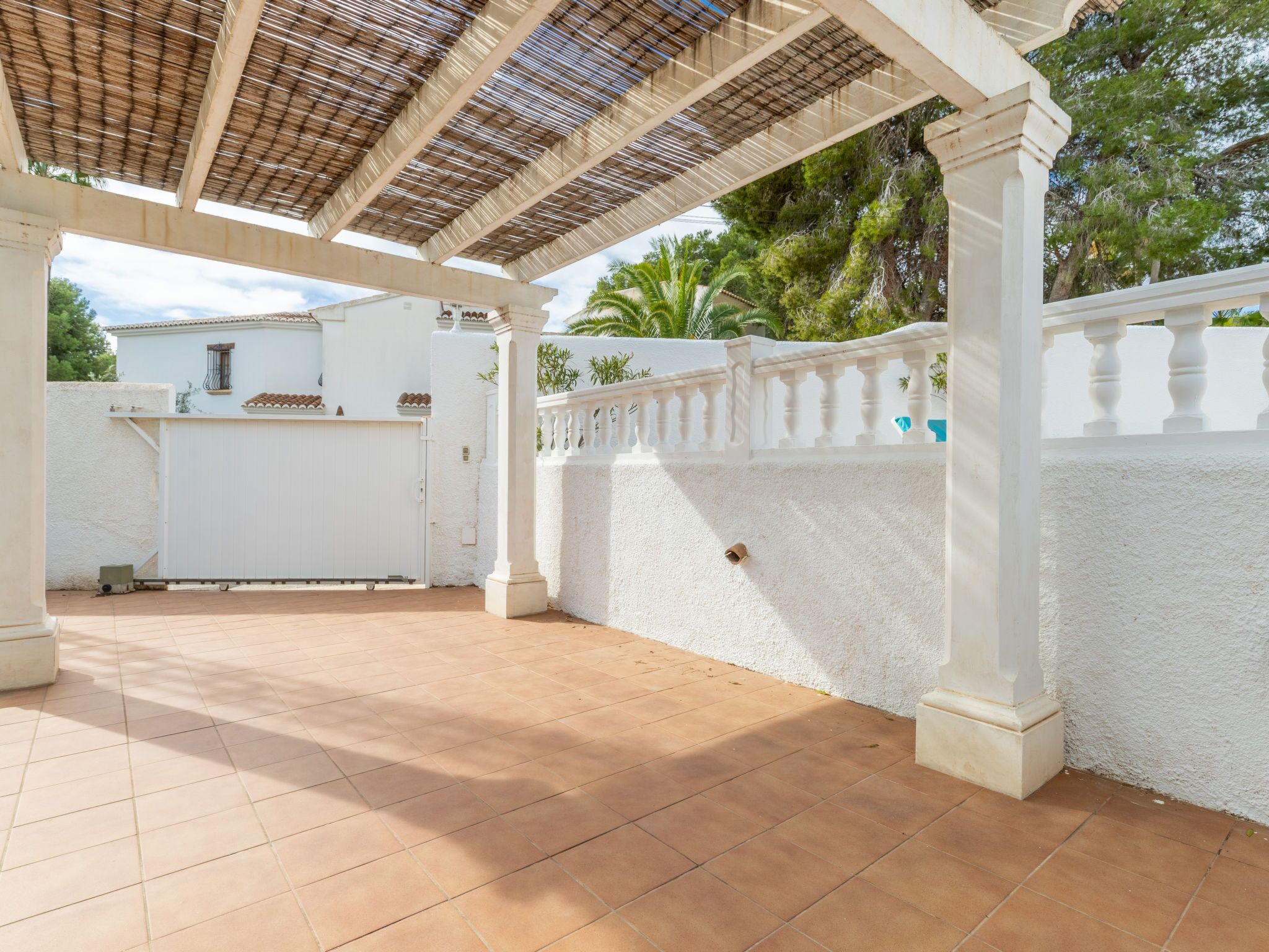 A covered patio area with tiled flooring, white walls, and a metal roof.