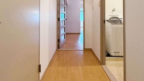 Un pasillo estrecho con suelo de madera y paredes blancas que conduce a una habitación con lavadora.