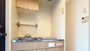 Een keuken met een roestvrijstalen spoelbak, een inbouwoven en een magnetron. Daarboven bevindt zich een houten kastje en aan de witte muur een thermostaat en een stopcontact.