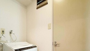 Een kleine kamer met een witte wasmachine, een deur en een ventilatie rooster aan de muur.